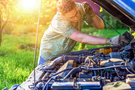 A guy repairs a motor of car at sunset in a country areaの写真素材