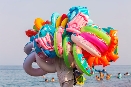 A seller with a bunch of different rubber rings and inflatable life-saving equipment strolls along the beachの写真素材