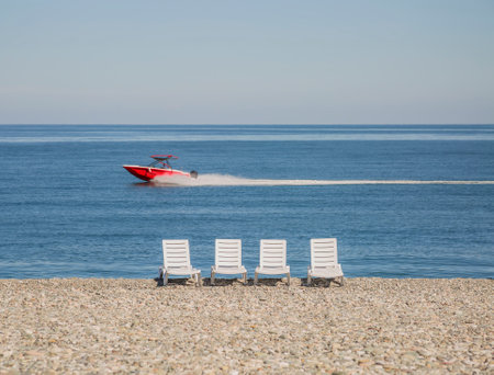 White deck chairs on a pebble beach by the sea. Red Speedboatの写真素材