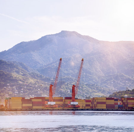 Seascape with orange loading port cranes and stacks of containers against the background of mountains in the morning sunの写真素材