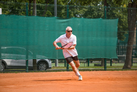An elderly man playing tennis runs to take the ball. Open ground.の写真素材