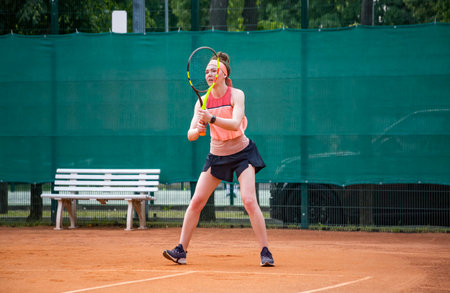 A young woman playing tennis is getting ready to take the ball in the center position. Open ground.の写真素材