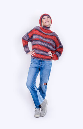 An adult woman dressed in blue jeans, a knitted terracotta sweater and a hat on a white background. Full lengthの写真素材