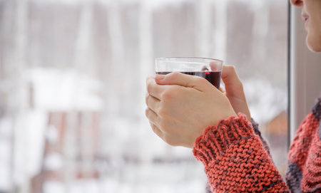 A woman stands at the window with a cup of mulled wine in his handの写真素材