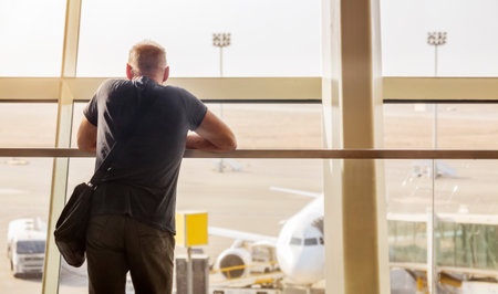 A man looks at a plane through a glass wall at the airportの写真素材