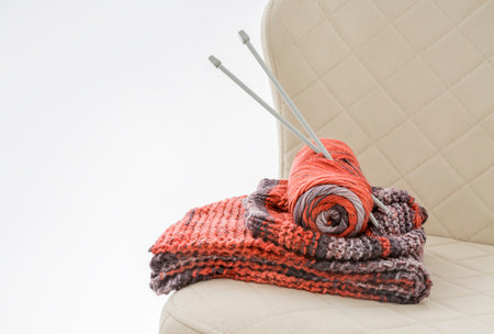 A ready-made knitted set and knitting needles stuck in a skein of yarn are folded on a chairの写真素材