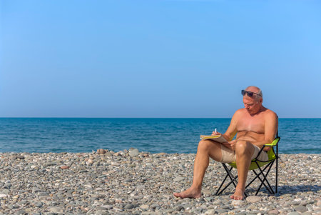 An elderly man does crossword puzzles on the beachの写真素材