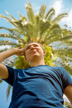 Portrait of a guy against the background of a palm tree crown framing his head like a festival wreath. Low view. Close-upの写真素材