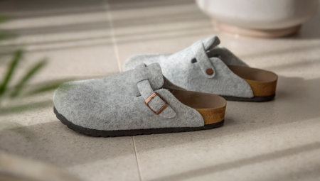 Grey felt slippers with cork soles stand on a beige stoneware floor. Modern, light-colored, sunny...
