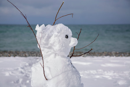 A snowman in close-up on the background of a snow-covered beach by the sea