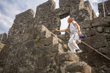 A woman in a white T-shirt and trousers runs up the stairs of an ancient fortressの写真素材