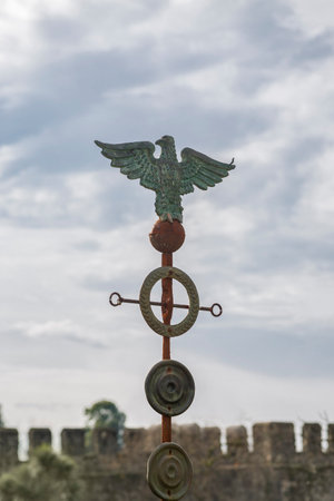 An ancient Roman eagle, covered with rust and patina, against a cloudy skyの写真素材