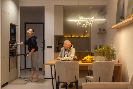 An adult woman takes out a baking dish with a ready-made pie from the built-in oven, intending to have tea with an elderly man who is waiting forの写真素材