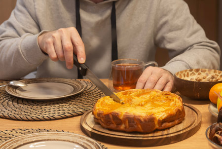 A man cuts a piece of pie while sitting at the dining table. Home food. Tea timeの写真素材