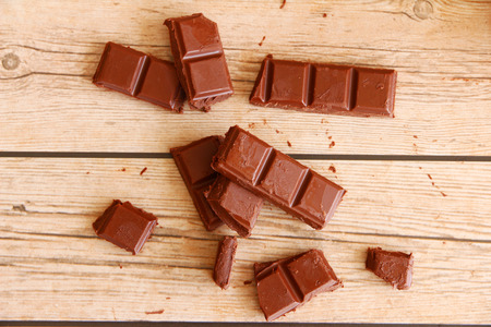 An arrangement of broken milk chocolate blocks, shot overhead on a rustic worn wooden background,...