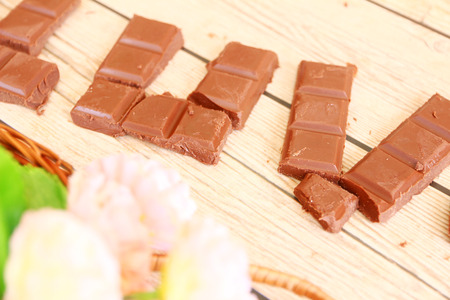 An arrangement of broken milk chocolate blocks, shot overhead on a rustic worn wooden background,...