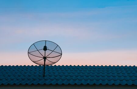 Silhouetted satellite dish on the roof in sunset skyの写真素材