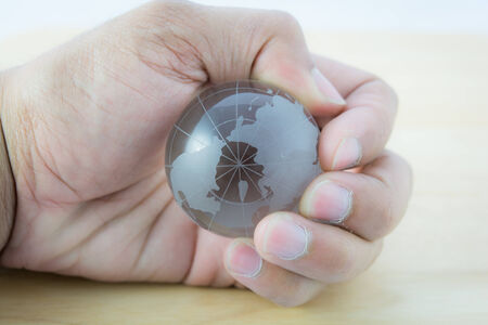 Glass the world in hand on wooden background