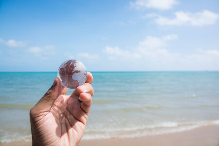 hand holding glass globe with beautiful beach view の写真素材