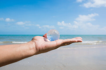 hand holding glass globe with beautiful beach view の写真素材