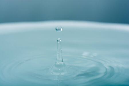 Water drop falling into water making dropletの写真素材