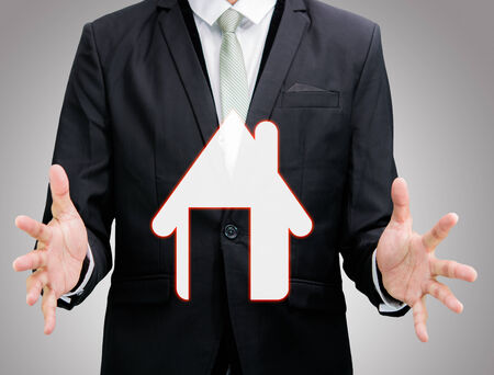 Businessman standing posture hand holding house icon isolated on over gray backgroundの写真素材