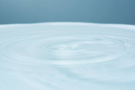 Water drop falling into water making dropletの写真素材