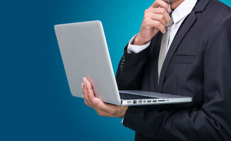 Businessman standing posture hand hold notebook laptop isolated on blue backgroundの写真素材
