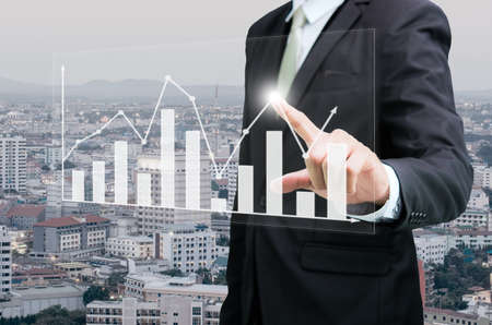 Businessman standing posture hand touch graph finance on City backgroundの写真素材