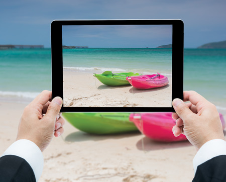 Businessman hands tablet taking pictures canoe on beach and seaの写真素材