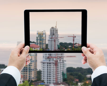 Businessman hands tablet taking pictures buildings under construction and cranes the seaの写真素材