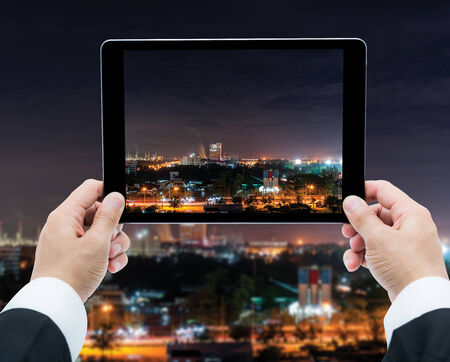 Businessman hands tablet taking pictures city skyscrapers night view at Chonburi Thailand