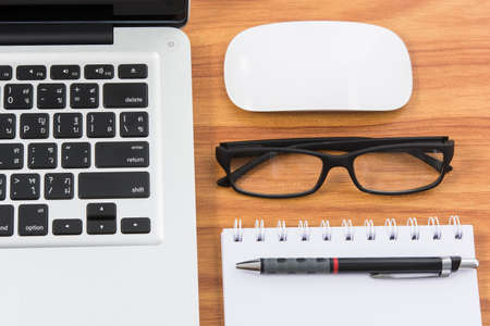 Blank business laptop, mouse, pen, note and glasses on wooden tableの写真素材