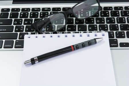 Blank business laptop, mouse, pen and glasses on white tableの写真素材