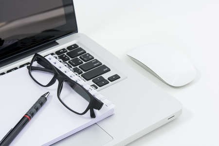 Blank business laptop, mouse, pen, glasses and note on white tableの写真素材