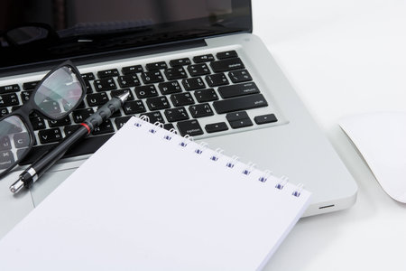 Blank business laptop, mouse, pen, glasses and note on white table