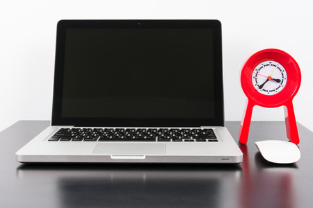 Laptop and red clock  on black wooden table on wall backgroundの写真素材