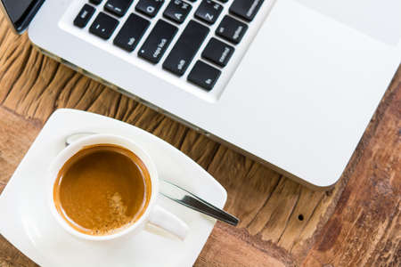 Coffee cup and laptop in coffee shop on wooden tableの写真素材