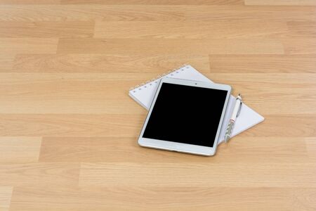 White digital Tablet on wooden table with pencil and book note