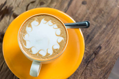 Yellow cup of coffee on wooden backgroundの写真素材