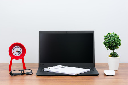 Black laptop on wooden table on white wallの写真素材