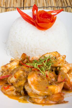 Curry fried shrimps and cooked rice in white dish closeup on table with wooden backgroundの写真素材