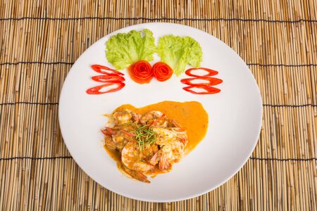 Curry fried shrimps and cooked rice in white dish closeup on table with wooden backgroundの写真素材