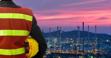 Hand or arm of engineer hold yellow plastic helmet in front of oil refinery industry