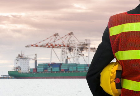Hand or arm of engineer hold yellow plastic helmet in front of cargo port loadingの写真素材