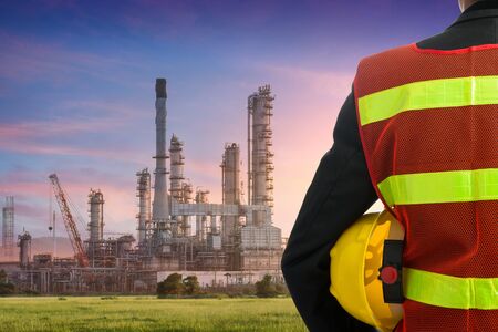 Hand or arm of engineer hold yellow plastic helmet in front of oil refinery industryの写真素材