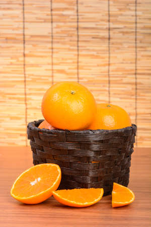 Oranges fruit in black basket on wood table with wooden backgroundの写真素材