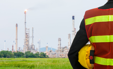 Hand or arm of engineer hold yellow plastic helmet in front of oil refinery industryの写真素材