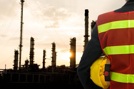 Hand or arm of engineer hold yellow plastic helmet in front of oil refinery industryの写真素材
