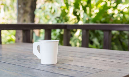 Coffee cup on wood table in cafe tree garden with bokeh light backgroundの写真素材